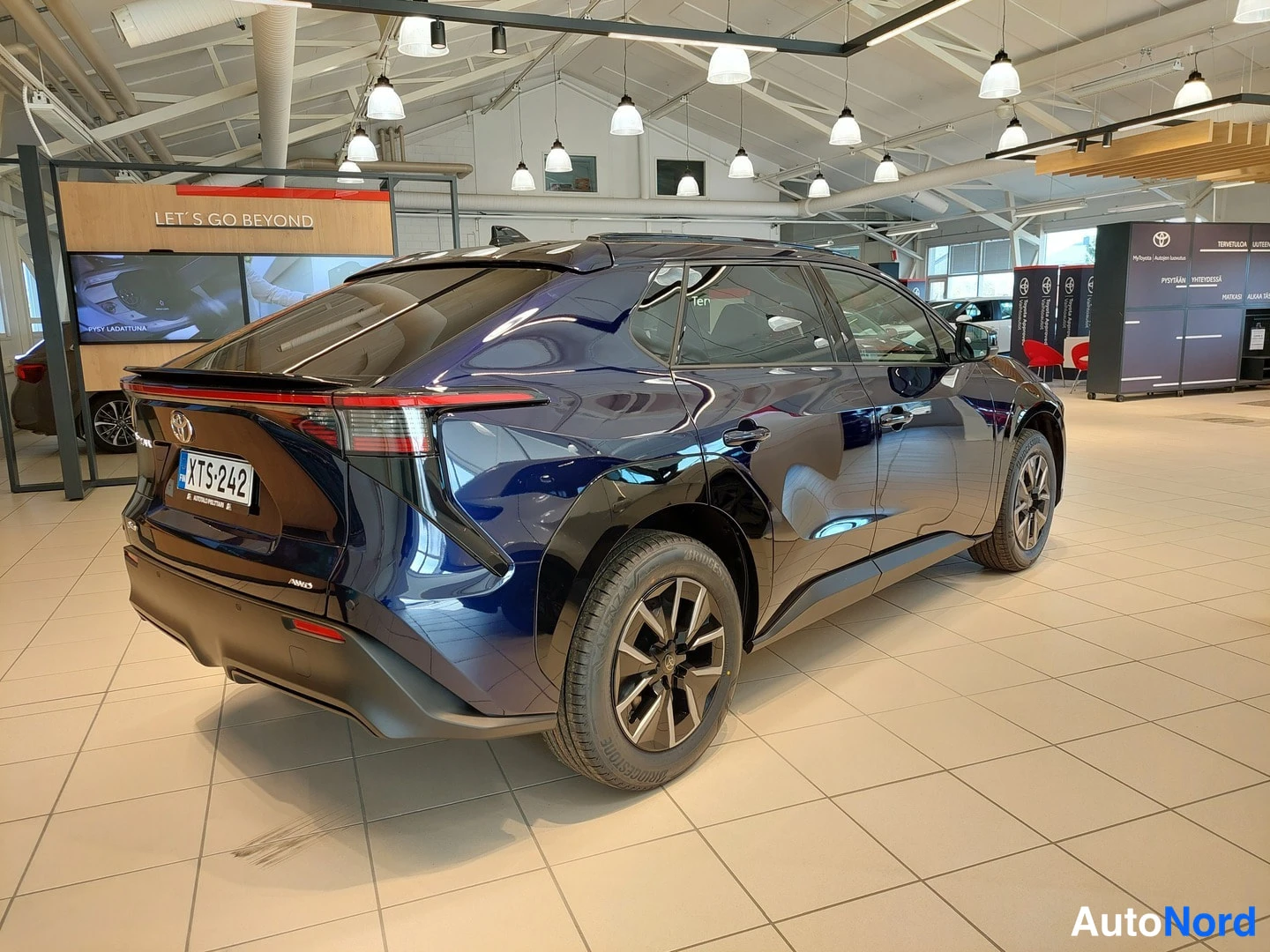 Takaviisto: Toyota BZ4X tummansinisenä taka- ja sivunäkymästä autosalon näyttelytilassa; takavalo ja rekisteritunnus näkyvissä.