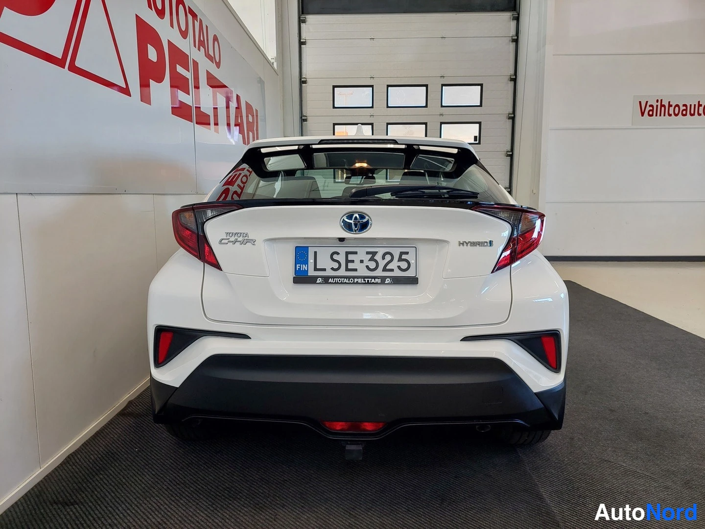 Takaa: Takaa suoraan otettu kuva valkoisesta hatchbackista; Toyotan logo, HYBRID-merkki, C-HR-kyltitys ja rekisterikilpi näkyvät.