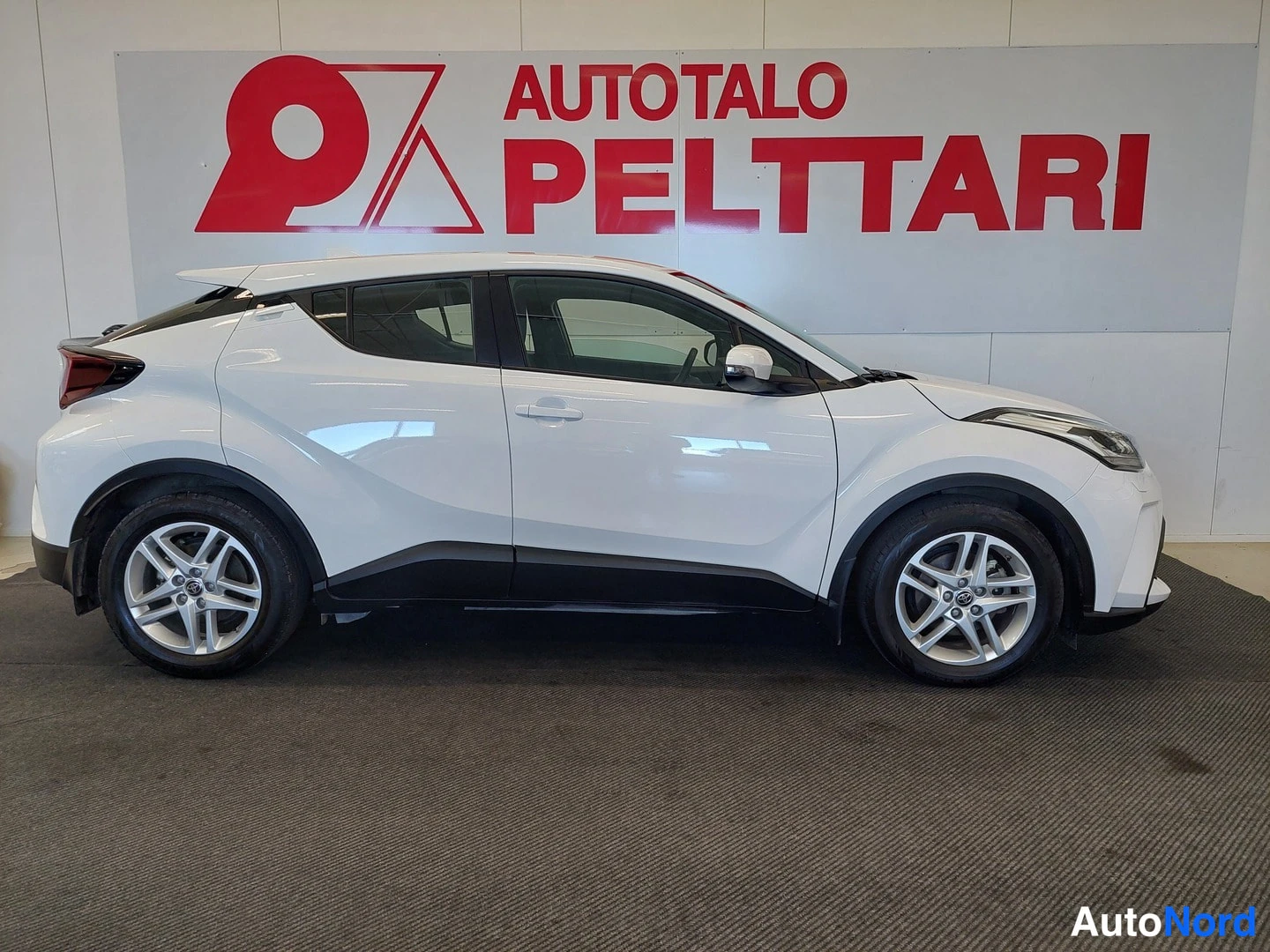 Etuviisto, nokka oikealle: Toyota C-HR:n etukolmasosan kuva: valkoinen korimuotoilu, mustat alareunat ja hopeavanteet esittelytilassa.