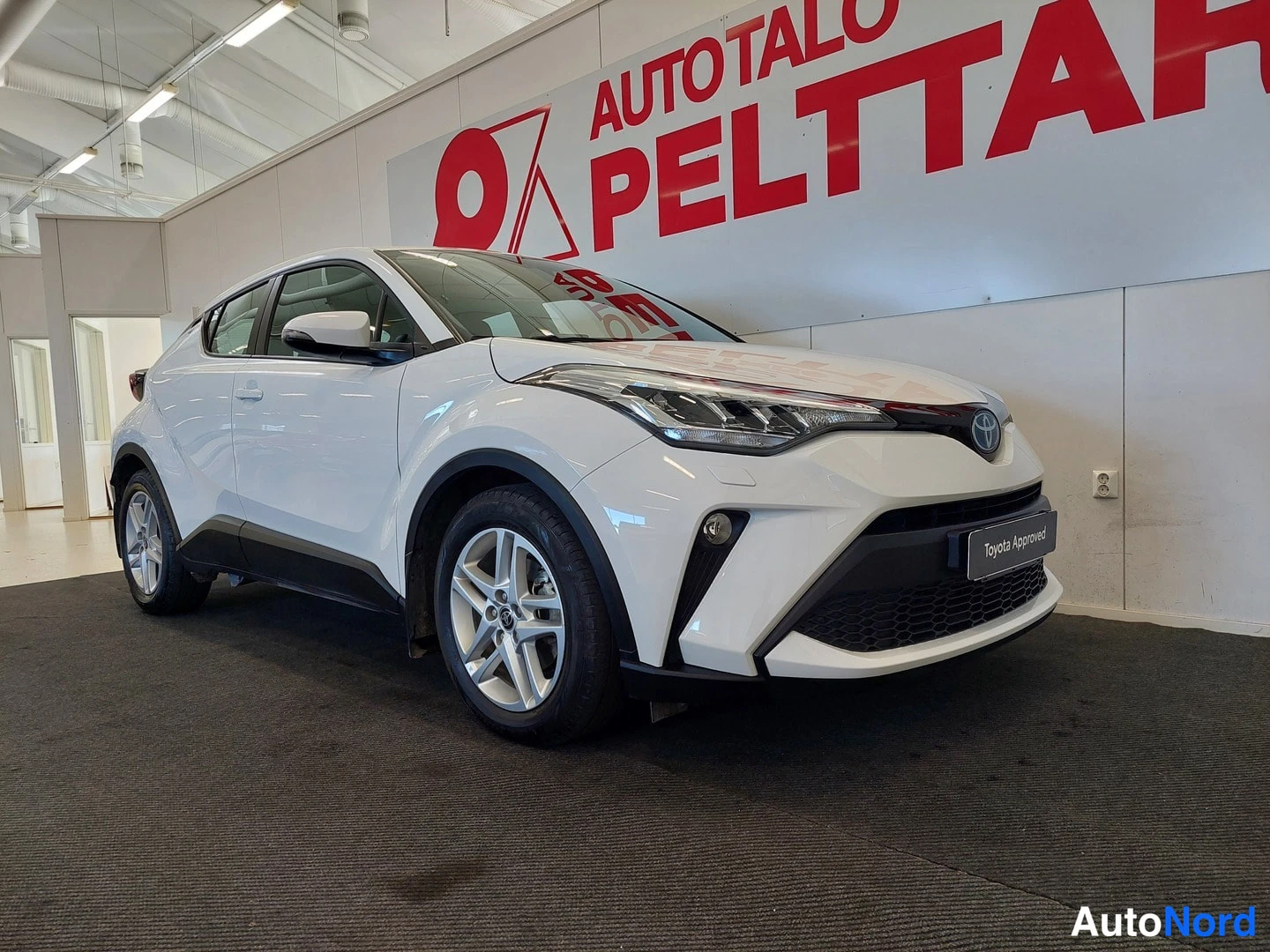 Etuviisto, nokka oikealle: Valkoinen Toyota C-HR etukulmasta oikealta sisätiloissa.