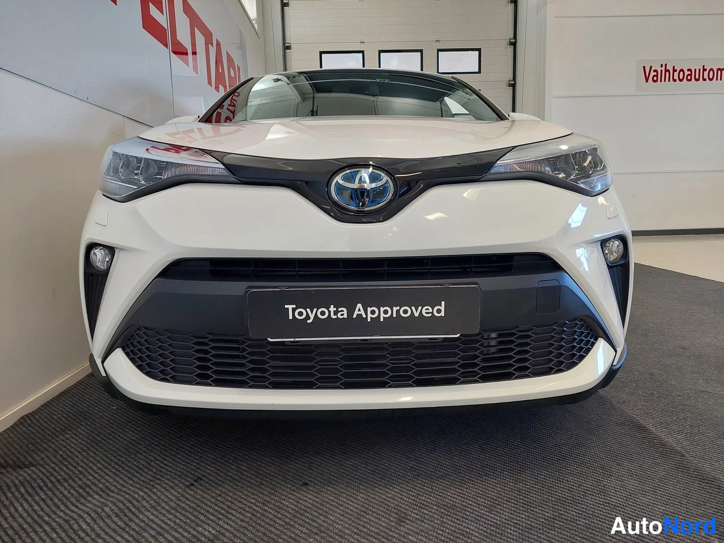 Edestä: Toyotan etupää suoraan edestä valkoisella korilla; keulalla Toyota-embleemi ja Toyota Approved -kilpi