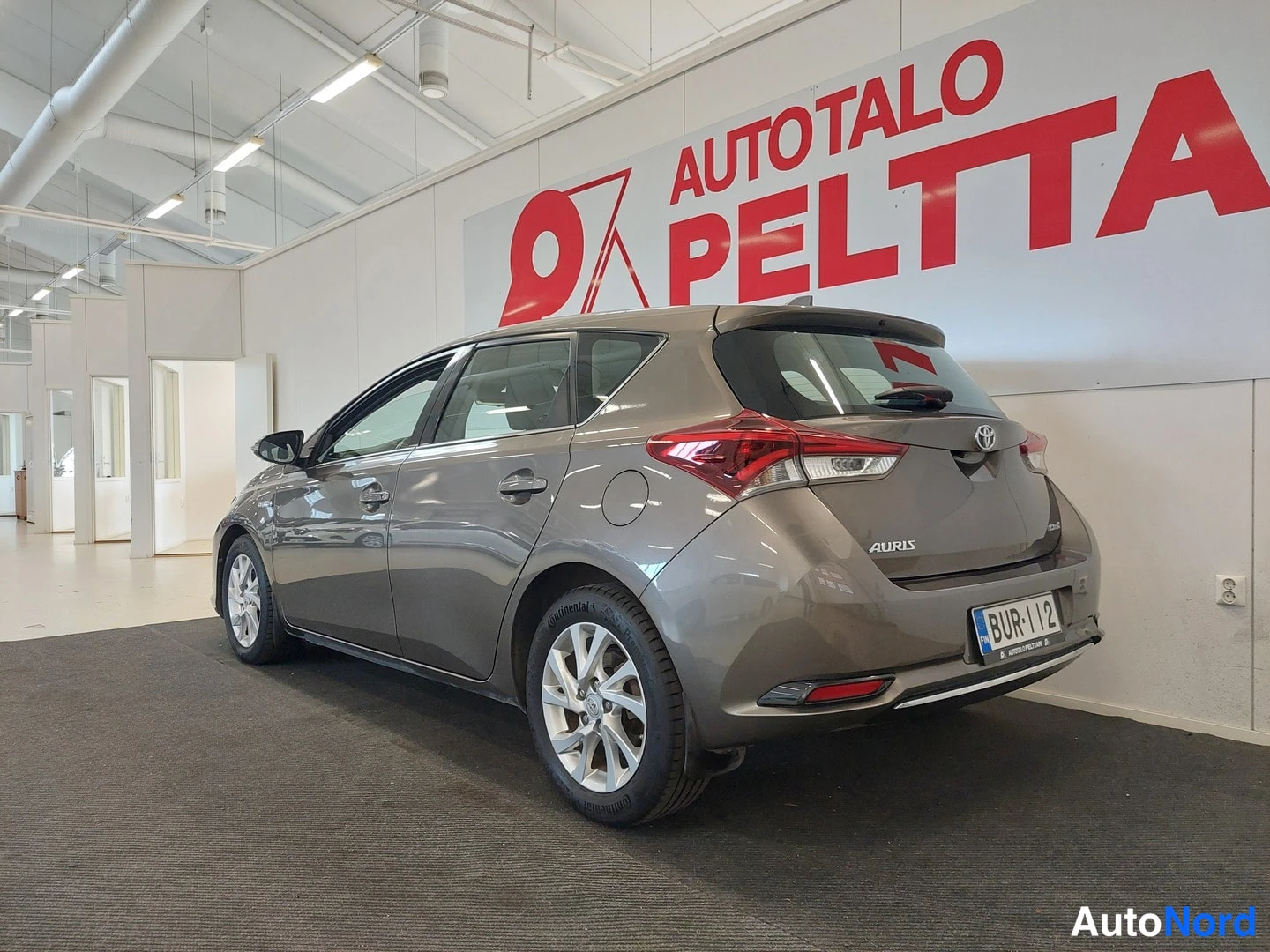 Takaviisto: Ruskeanharmaa Toyota Auris takaosa ja sivu näkyvätAutohallissa rekisterikilpi