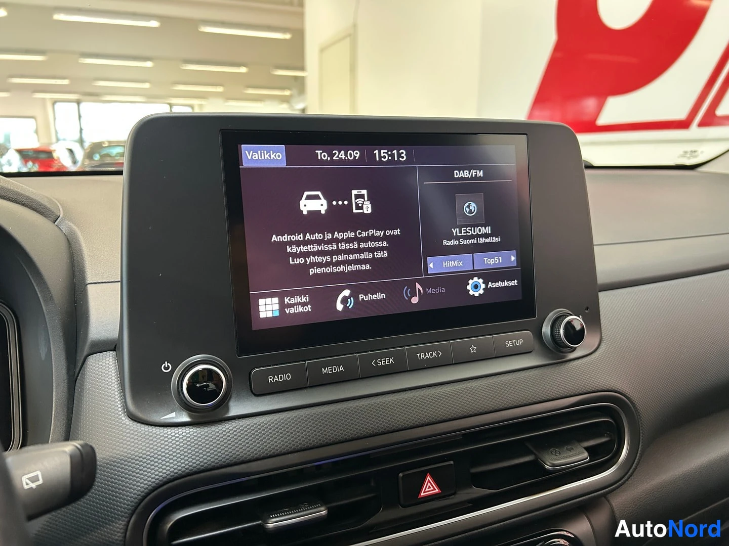 Muu: Keskikonsolin näyttö valikossa: teksti kertoo, että Android Auto ja Apple CarPlay ovat käytettävissä; DAB/FM-radio kanavalla Yleisuomi, kellonaika 15:13, päiväm