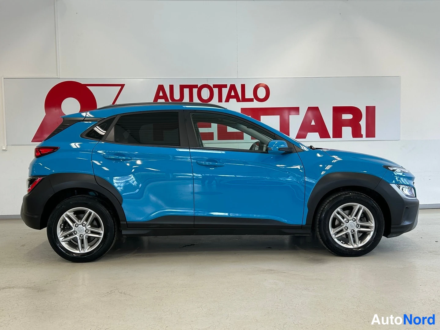 Sivulta: Sininen Hyundai Kona sivulta, vasen kylä näkyvissä.