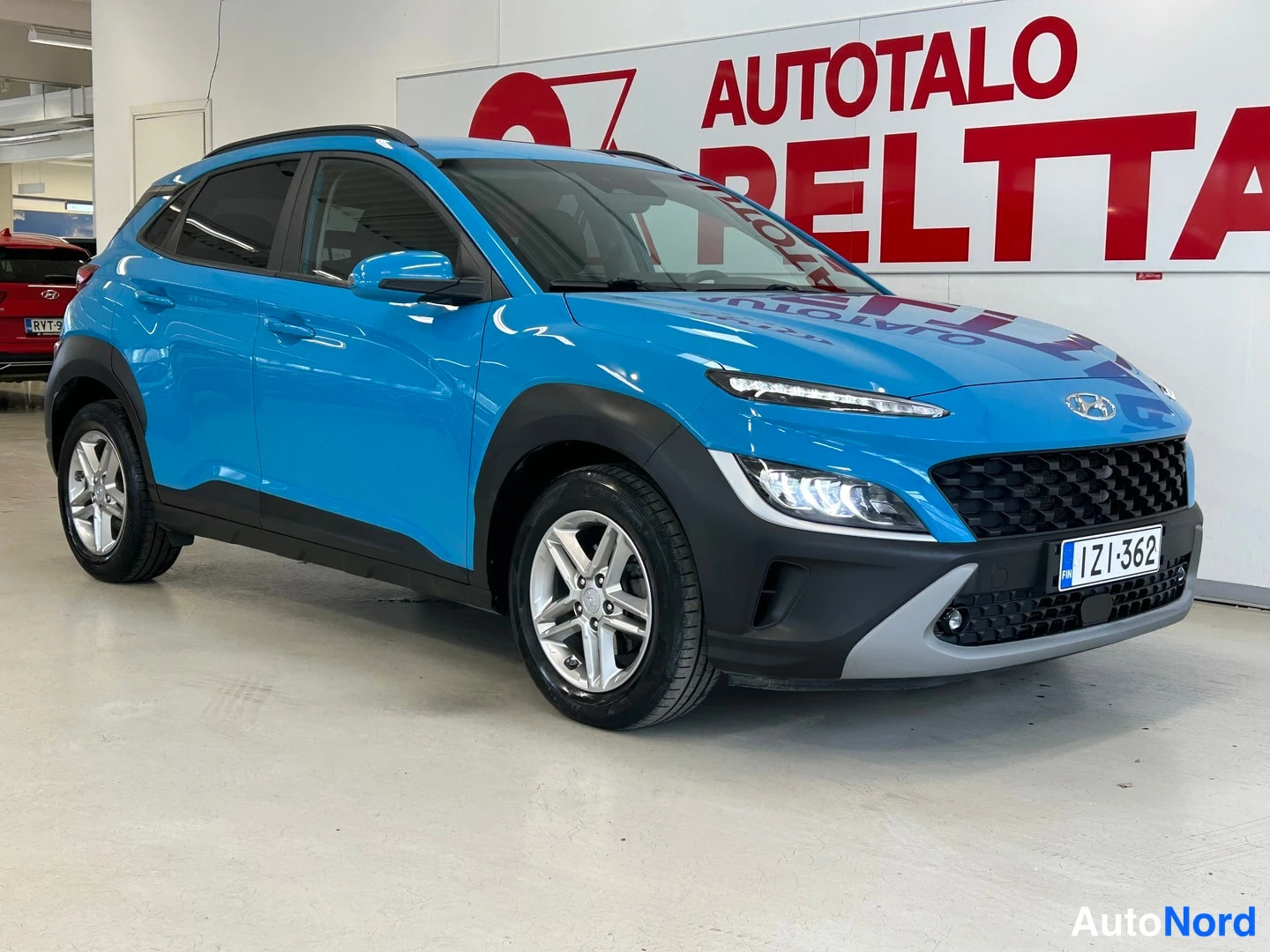 Etuviisto, nokka oikealle: Sininen Hyundai Kona etuosa ja vasen kylä kolmannelta neljännekseltä, keulakuva oikealla.