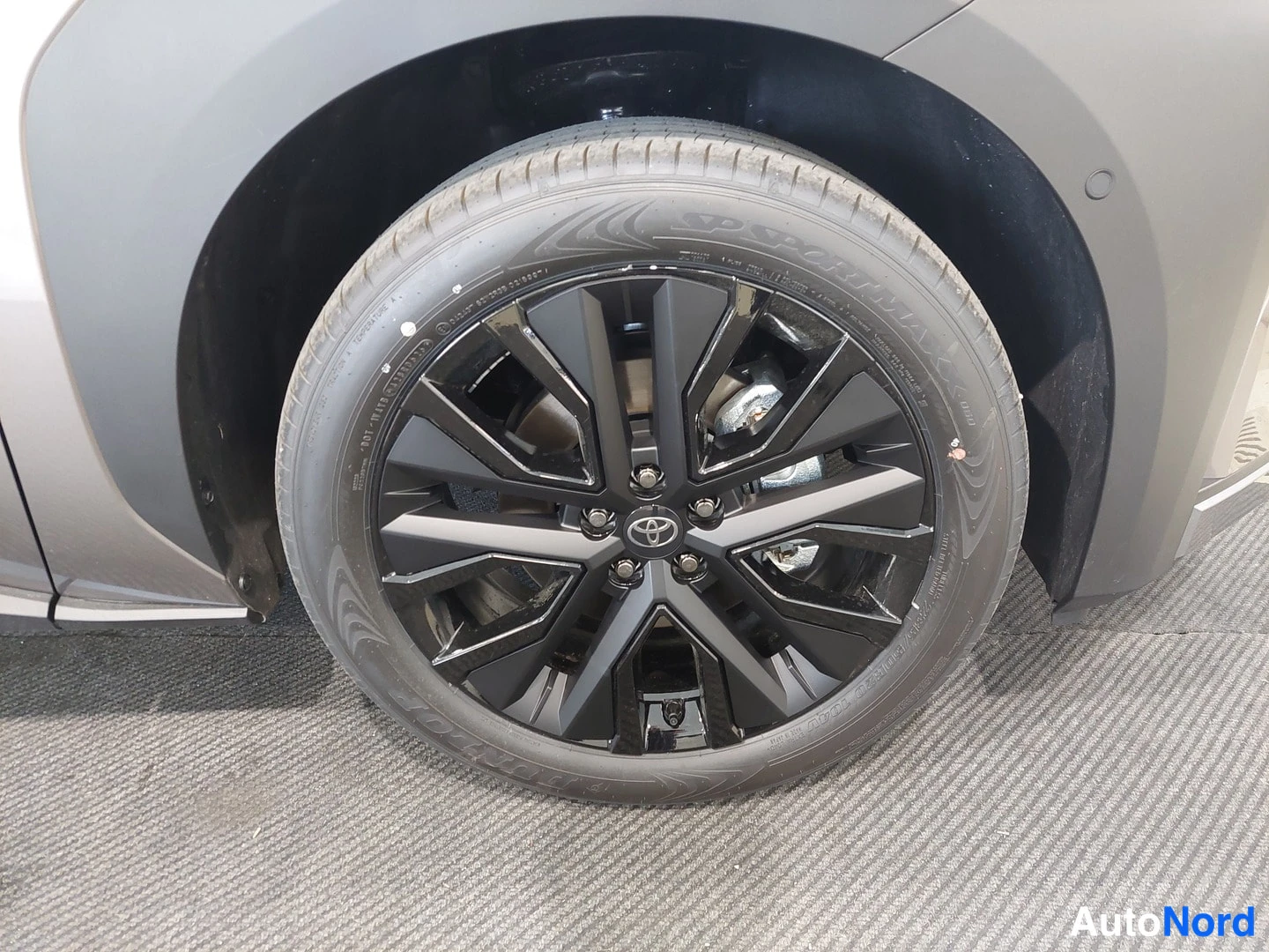 Muu: Auton pyörä lähikuvassa: musta pinnakevanteenvärinen metallivanne Toyota-embleemillä ja tire-tekstitys renkaan sivussa.