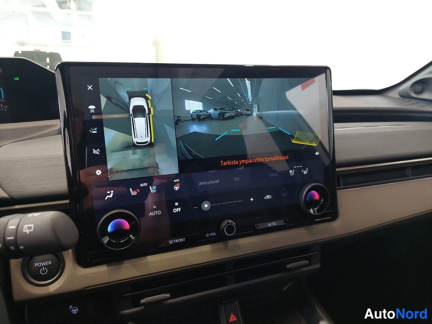Muu: Infotainment-näytön kuva näyttää ympärivaran 360°-kameranäkymän autosta ja tekstin 'Tarkista ympäristön turvallisuus' sekä lämpimyöden ja lämmityksen asetukset.