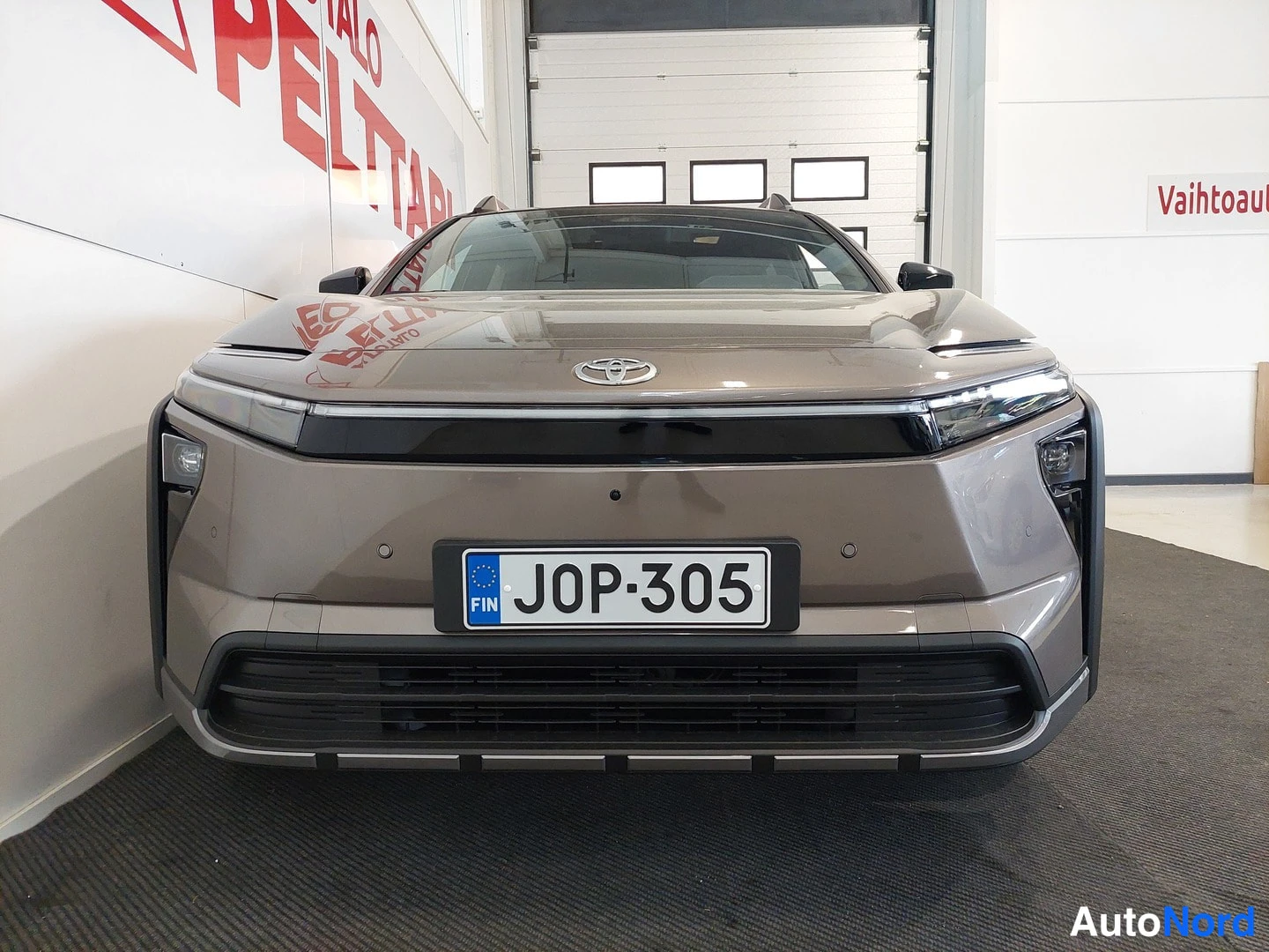 Edestä: Auton etunäkymä suoraan edestä: ruskeakarmaa Toyota bZ4X Touring, musta etusäleikkö ja rekisteritunnus.