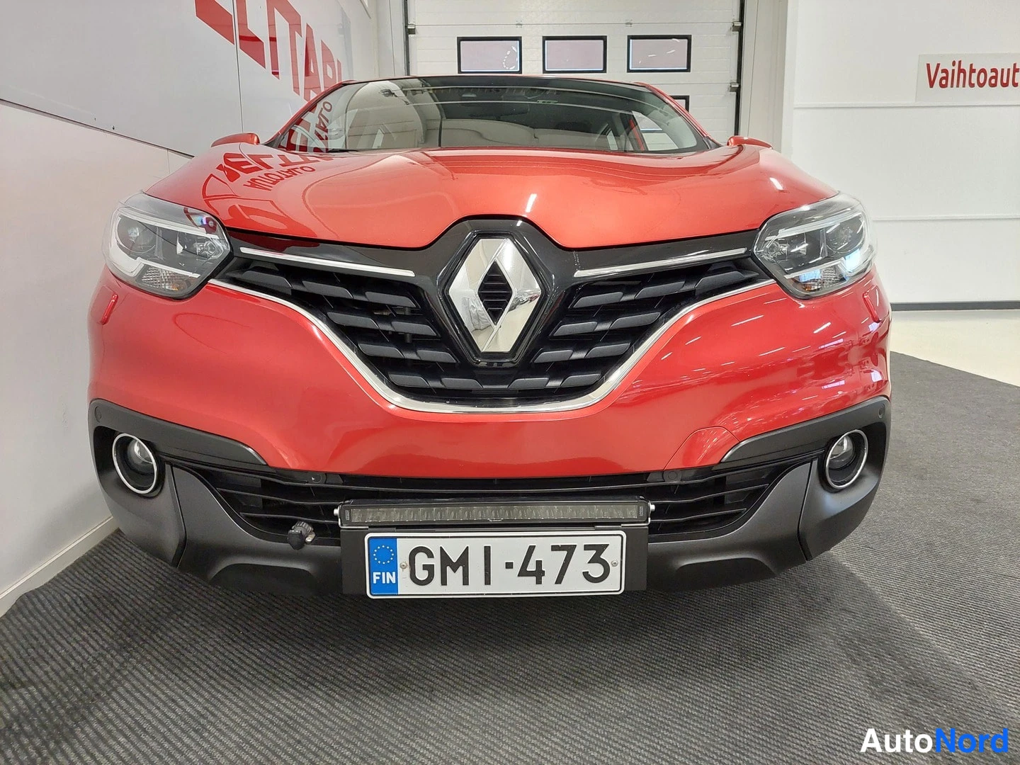 Edestä: Punaisen Renault Kadjar -henkilöauton etupää etusuoraalta; rekisterikilpi ja lisävalo puskurissa.