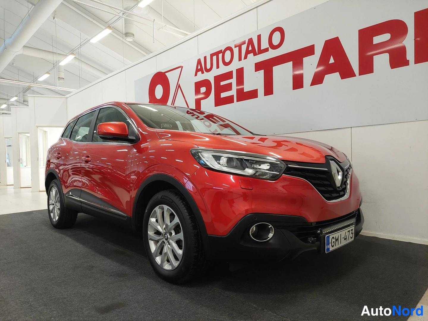 Etuviisto, nokka oikealle: Punaisen Renault Kadjarin etukulma sisätiloissa, etugrille ja rekisterikilpi näkyvissä.