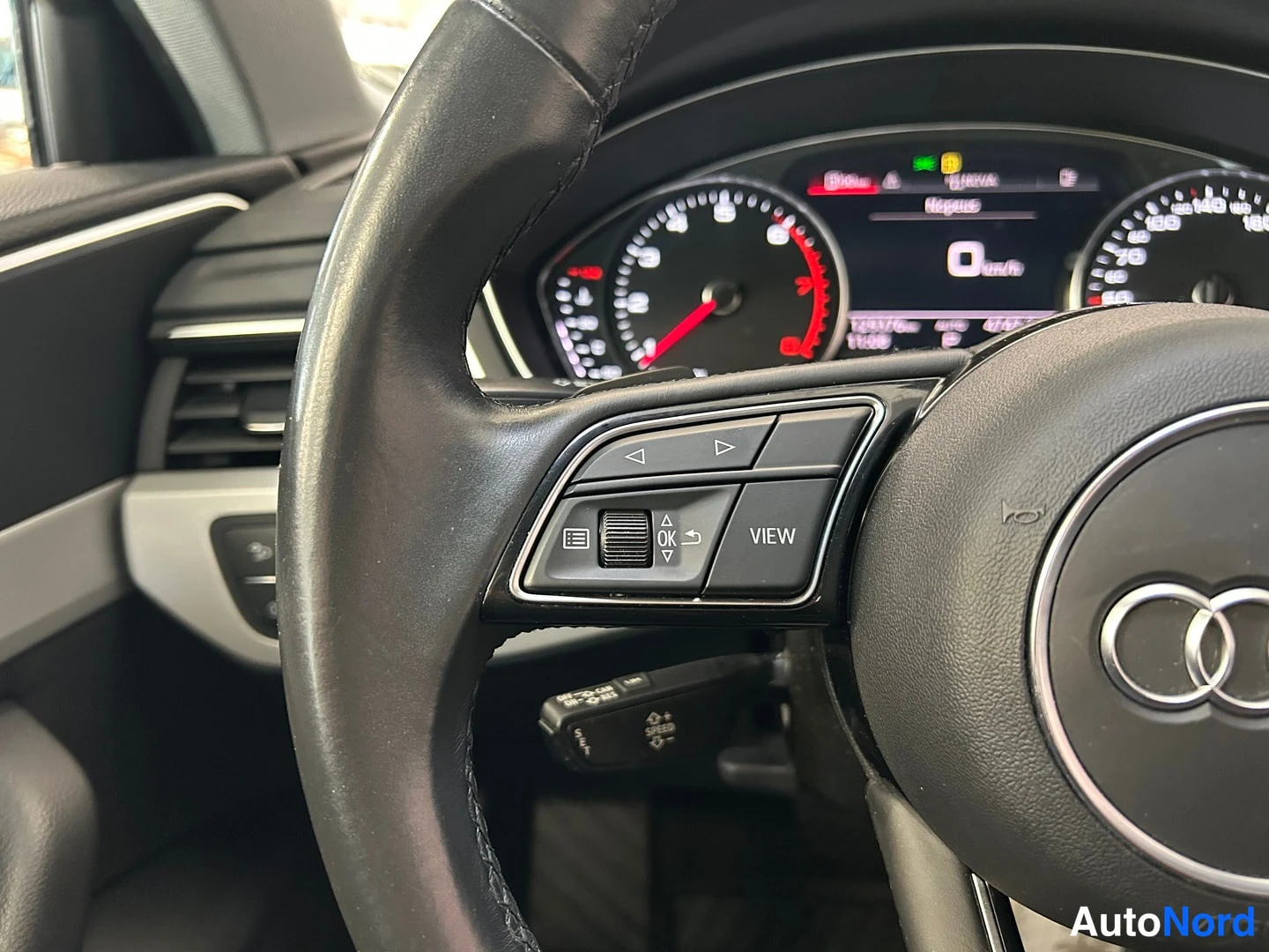Yksityiskohta: Audi A4:n ohjauspyörän vasemman puolen painikkeet VIEW- ja OK-näppäimillä lähikuvassa, taustalla mittaristo.