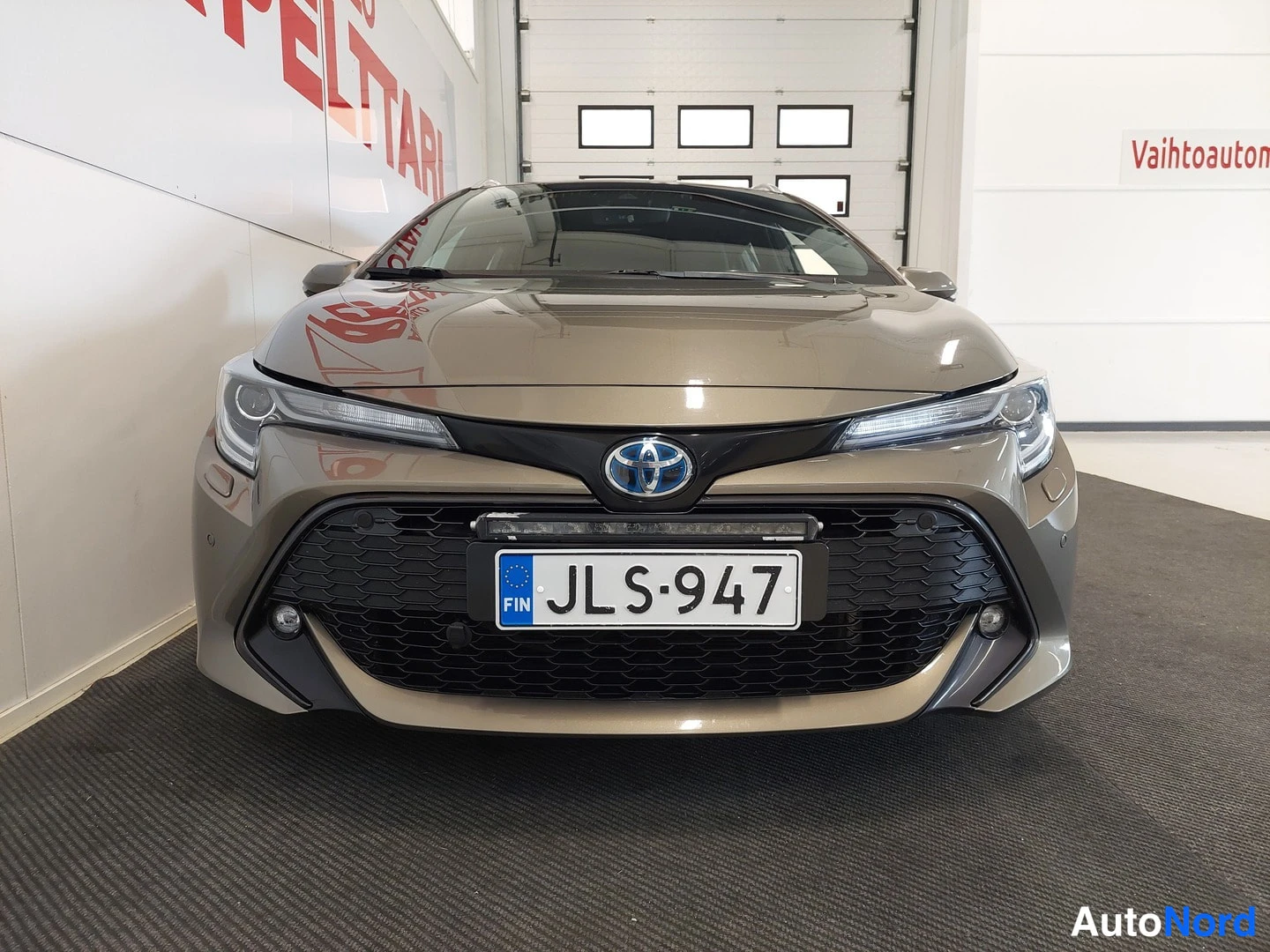 Edestä: Auton etuosasta suoraan otettu kuva: etusäleikkö, Toyota-merkki, A-levyillä otsavalo ja rekisteritunnus.
