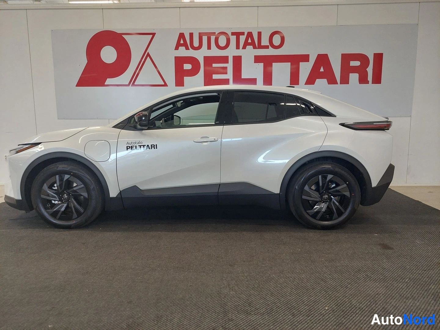 Sivulta: Auton sivuprofiili kokonaisuudessaan, valkoinen korinen SUV seinätekstin edessä.