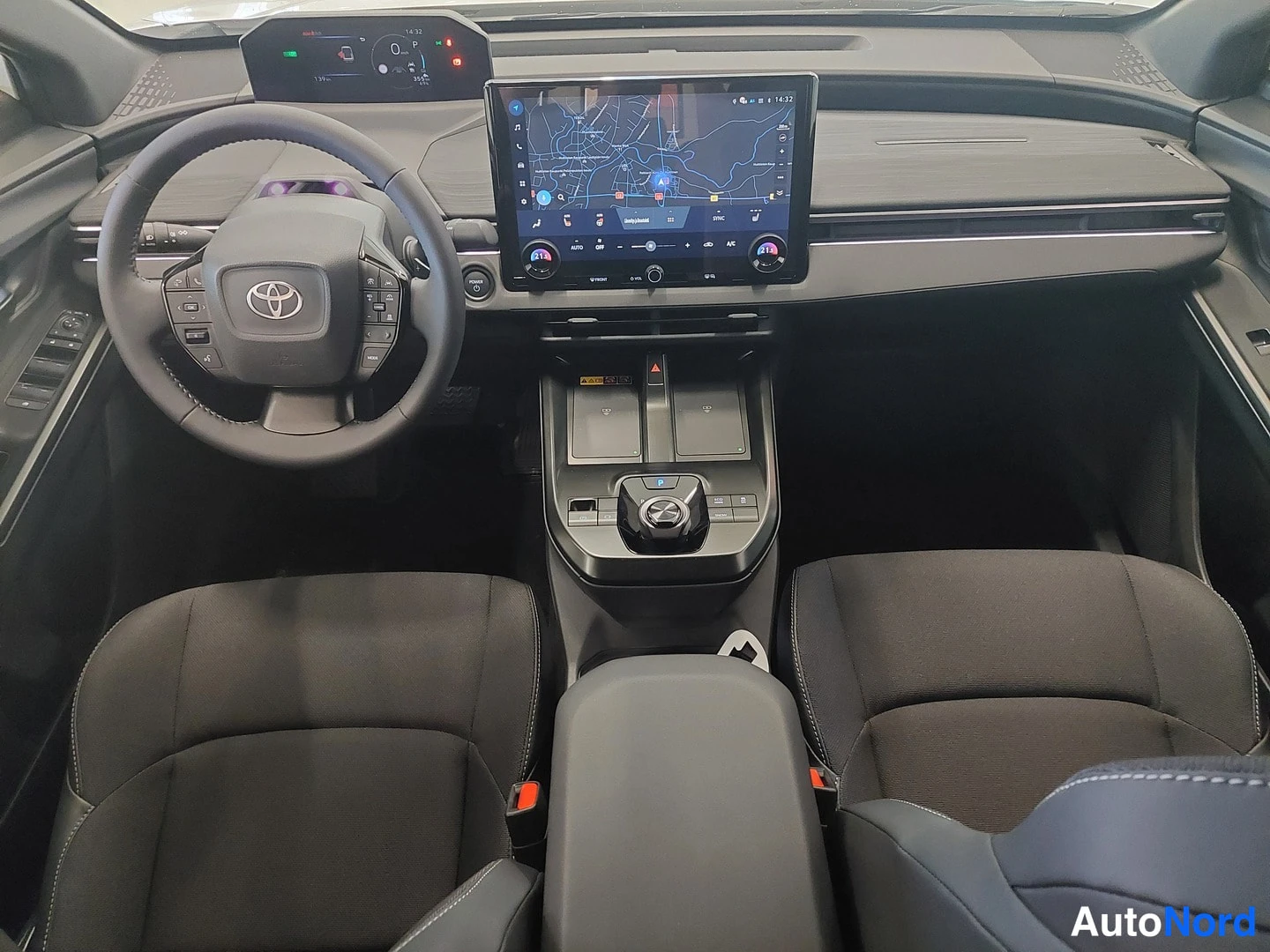 Takaa: Toyota C-HR:n tumma ohjaamo: ohjauspyörä, karttanayttö ja kaksi etuistuinta.