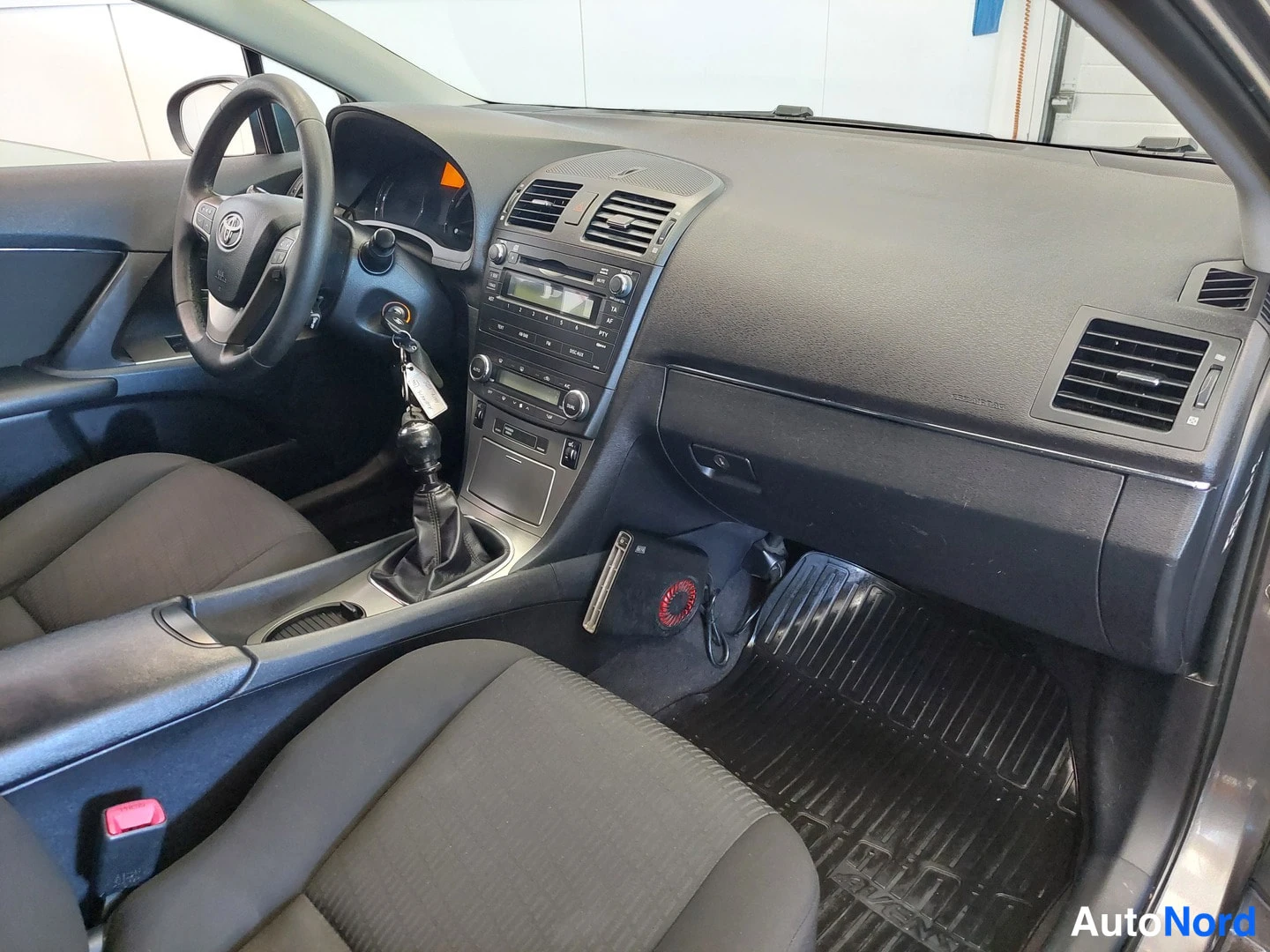 Muu: Ohjaamo vasemmalta: tumma kojelauta, Toyota-ohjauspyörä, manuaalivaihteen keila ja tummat kankaanistuimet.