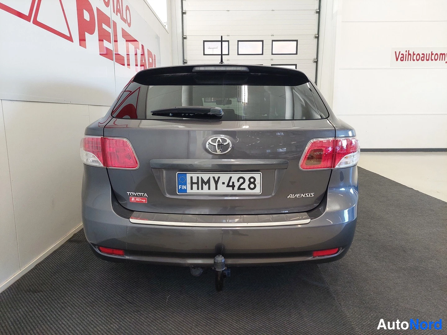 Takaa: Toyota Avensis -farmarin takaosa rekisterikilvellä ja vetoaimella, kuvattuna sisätiloissa.