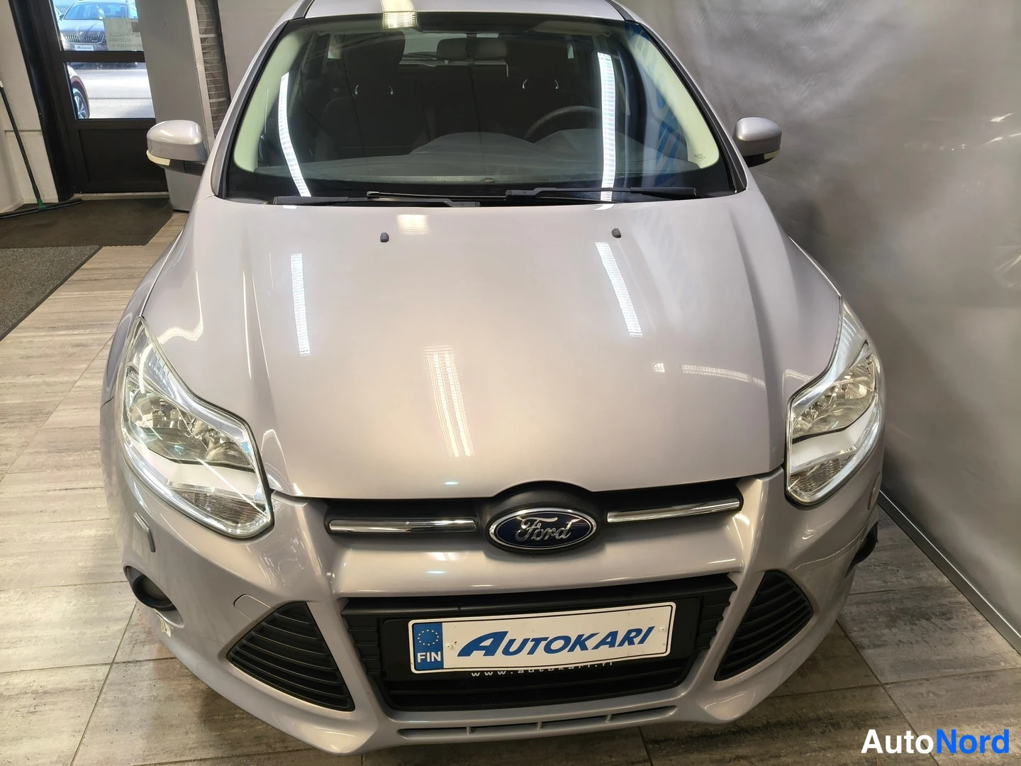 Edestä: Ford Focus -henkilöauto suoraan edestä: näkyvissä etusäleikkö Ford-merkki, ajovalot, etupuskuri ja Autokari-tekstinen kilvenkehus.