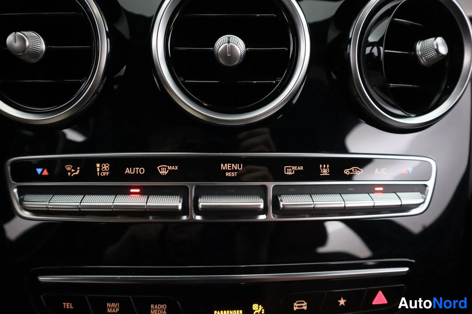 Yksityiskohta: Keskiöconsole ilmastointipaneeli: AUTO, MAX, REAR, A/C- ja muut painikkeet sekä kolme pyöreää tuuletusaukkoa.