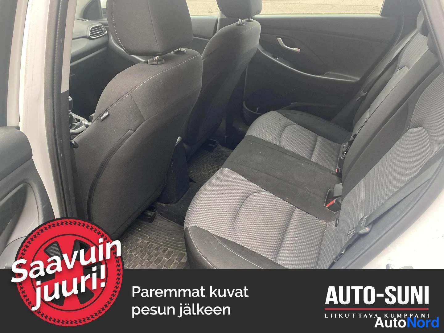 Yksityiskohta: Auton takaistuin tummalla kankaalla ja lavakaukalo matolla lattialla.