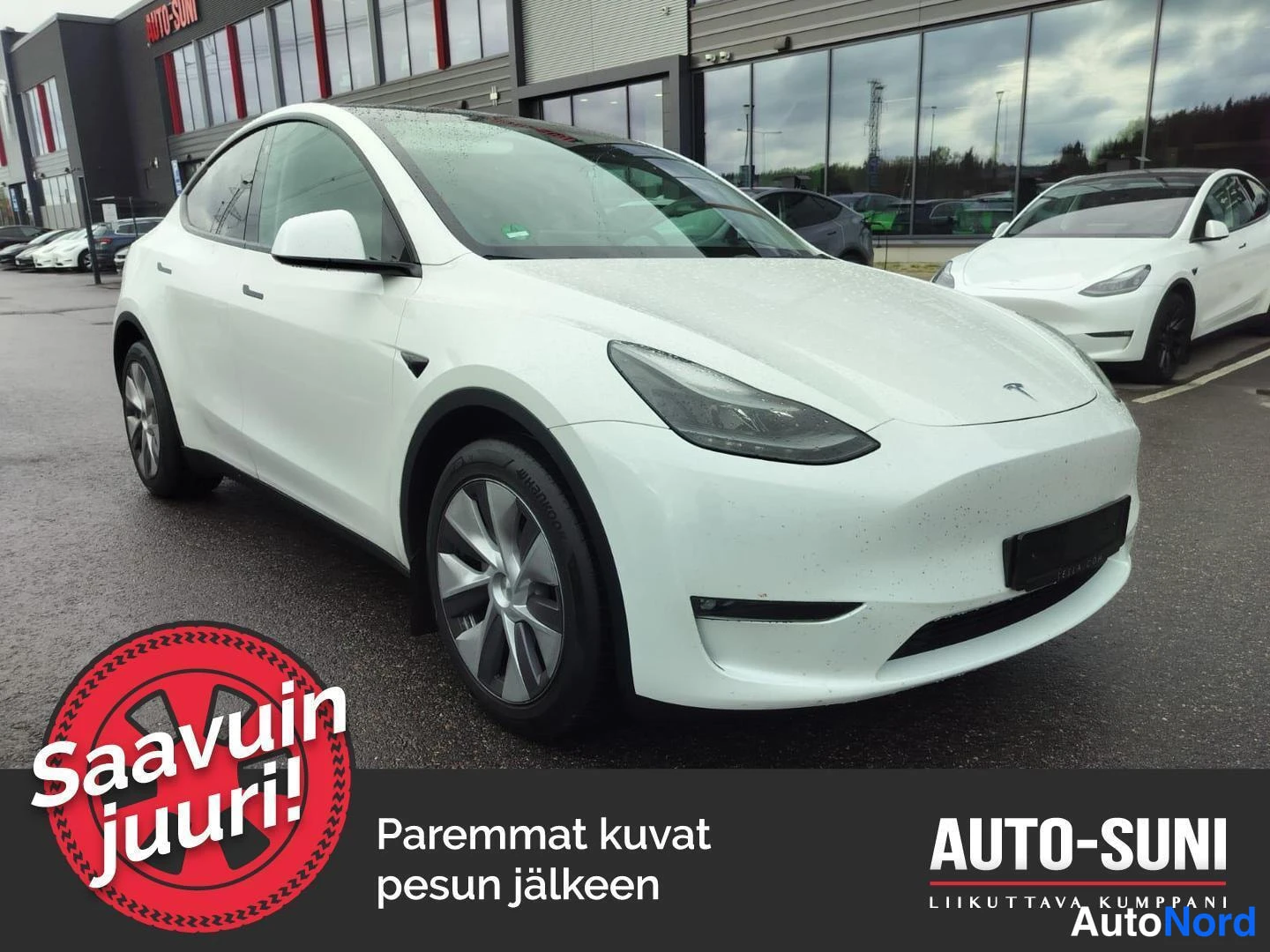 Etuviisto, nokka oikealle: Valkoinen Tesla Model Y etu-3/4-kulmakuva, keula oikealla, autopaikalla myyntihallin edessä.