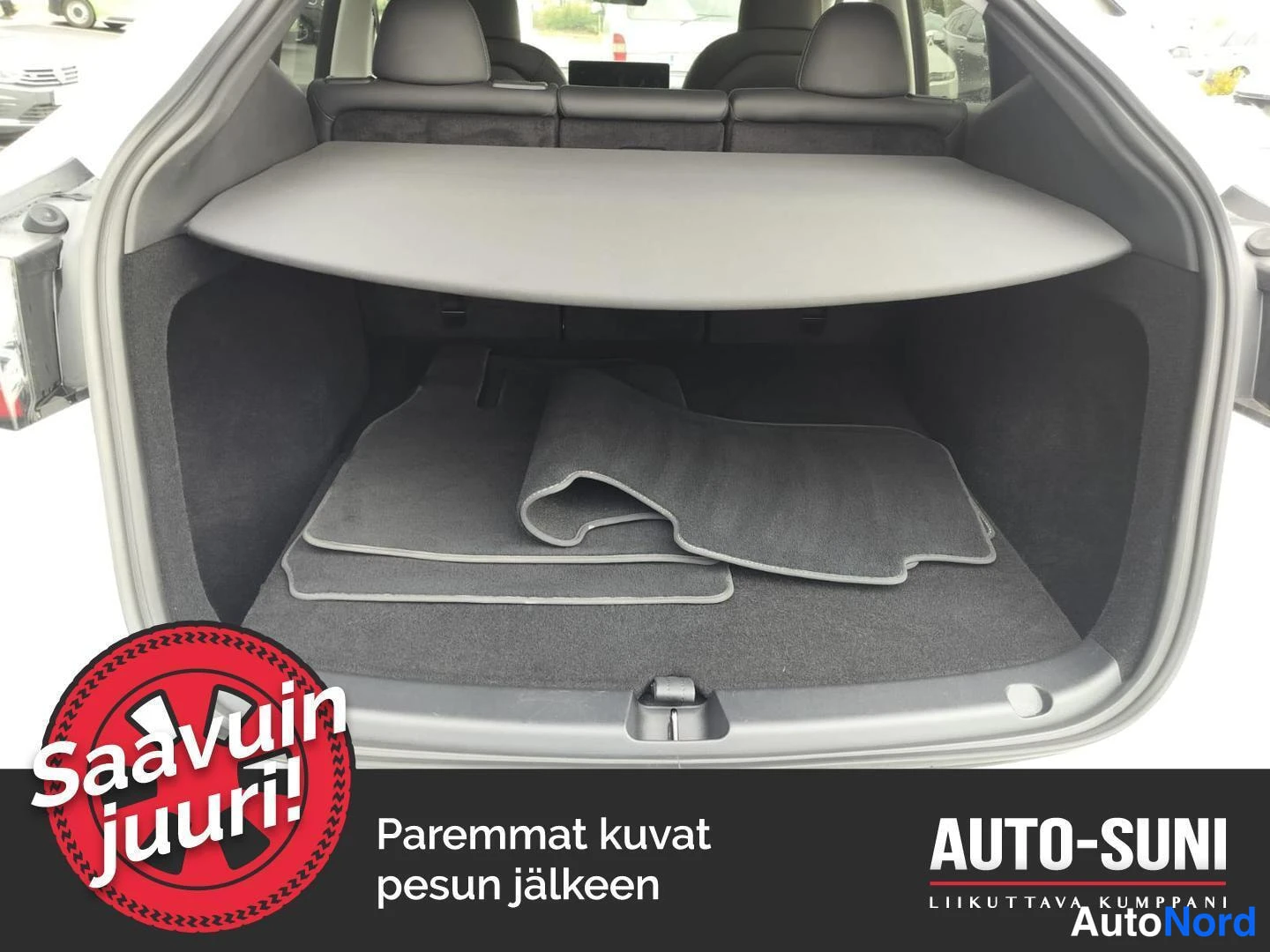 Yksityiskohta: Tavaratilan sisäkuva: tumma matto pohjalla, irto-matot rullalla ja sälekaitti taitettuna hyllylle, takapenkkien selkänojat taustalla.