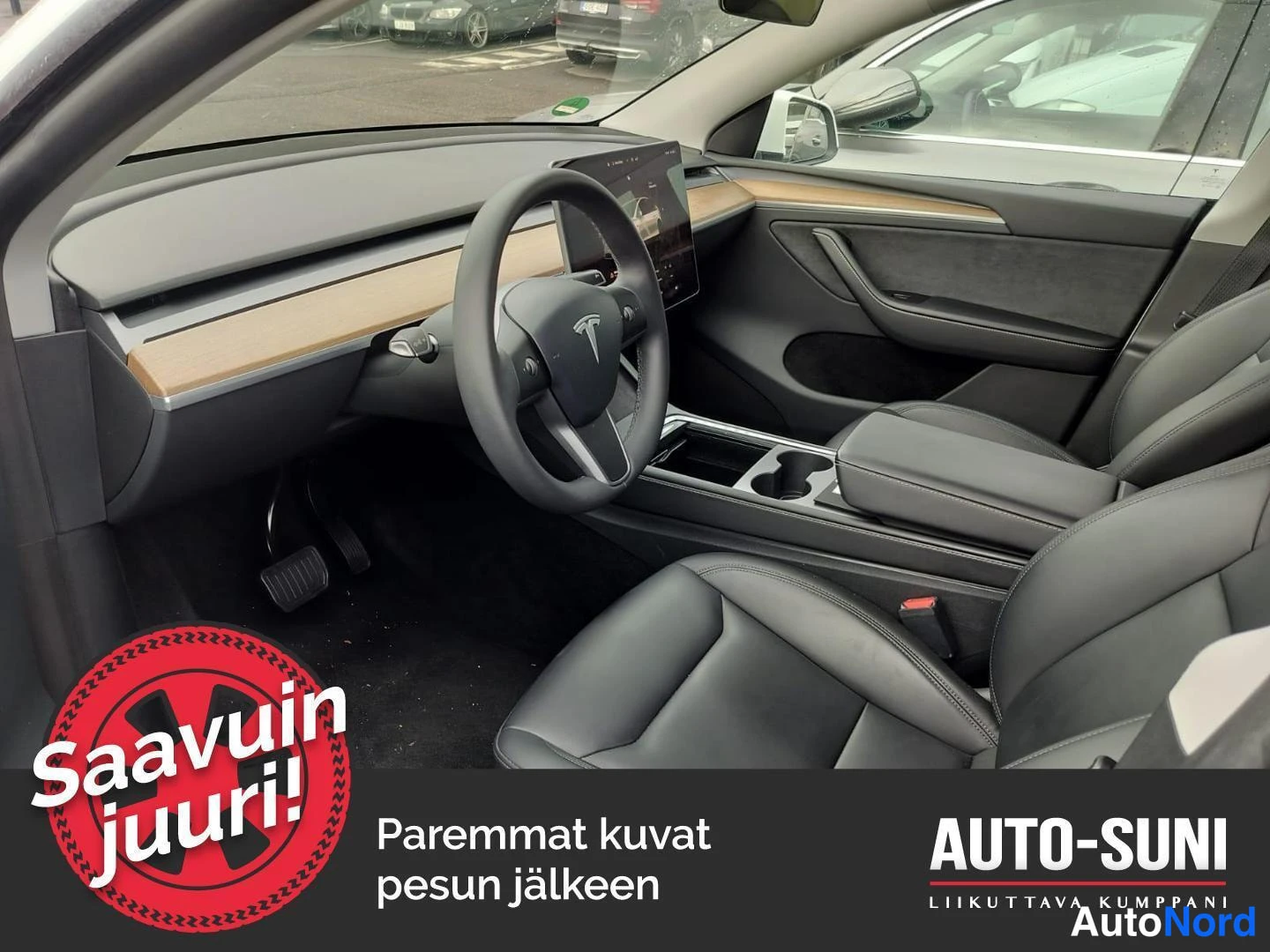 Muu: Autojen sisätilat: mustat penkit ja ohjauspyörä, keskellä iso näyttö, puunväriset koristelistat kojelaudassa.