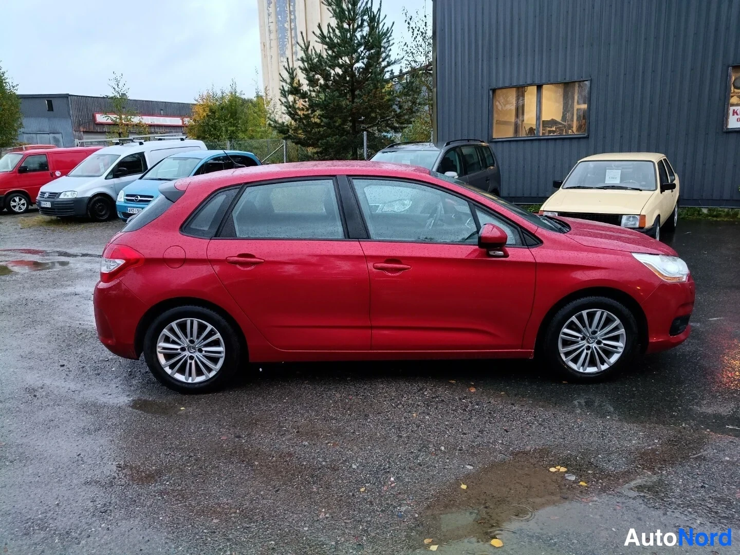 Sivulta: Citroën C4 -viistoperä punaisena sivulta kuvattuna, viides ovi ja molemmat kyljet näkyvissä sadealueella.
