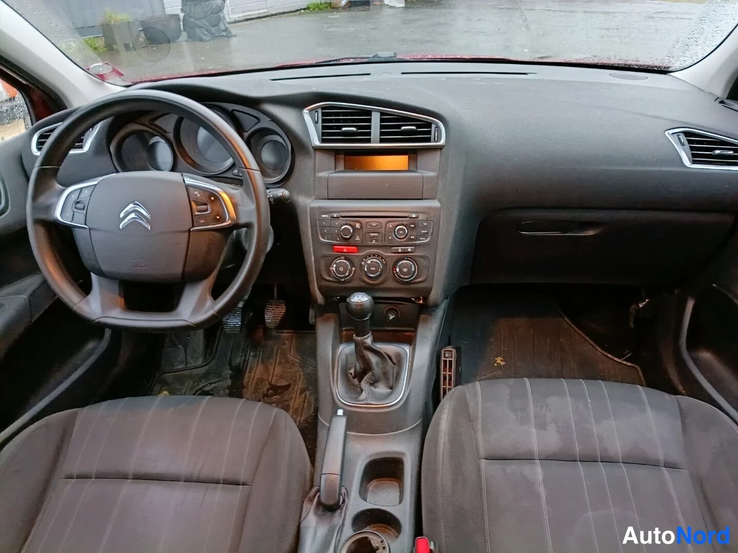 Muu: Citroën C4:n ohjaamo etuistuinten takaa: ratissa Citroën-logo, manuaalivaihteen keila ja tummat kangasistuimet.