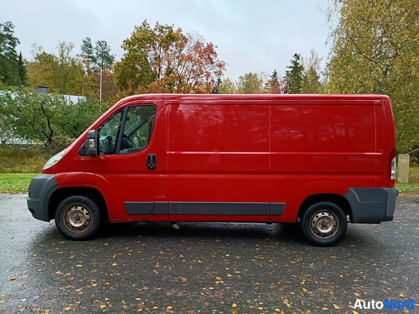 Sivulta: Punaisen pakettiauton sivuprofiili vasemmalta, suljetut takaovet ja teräsvanteet