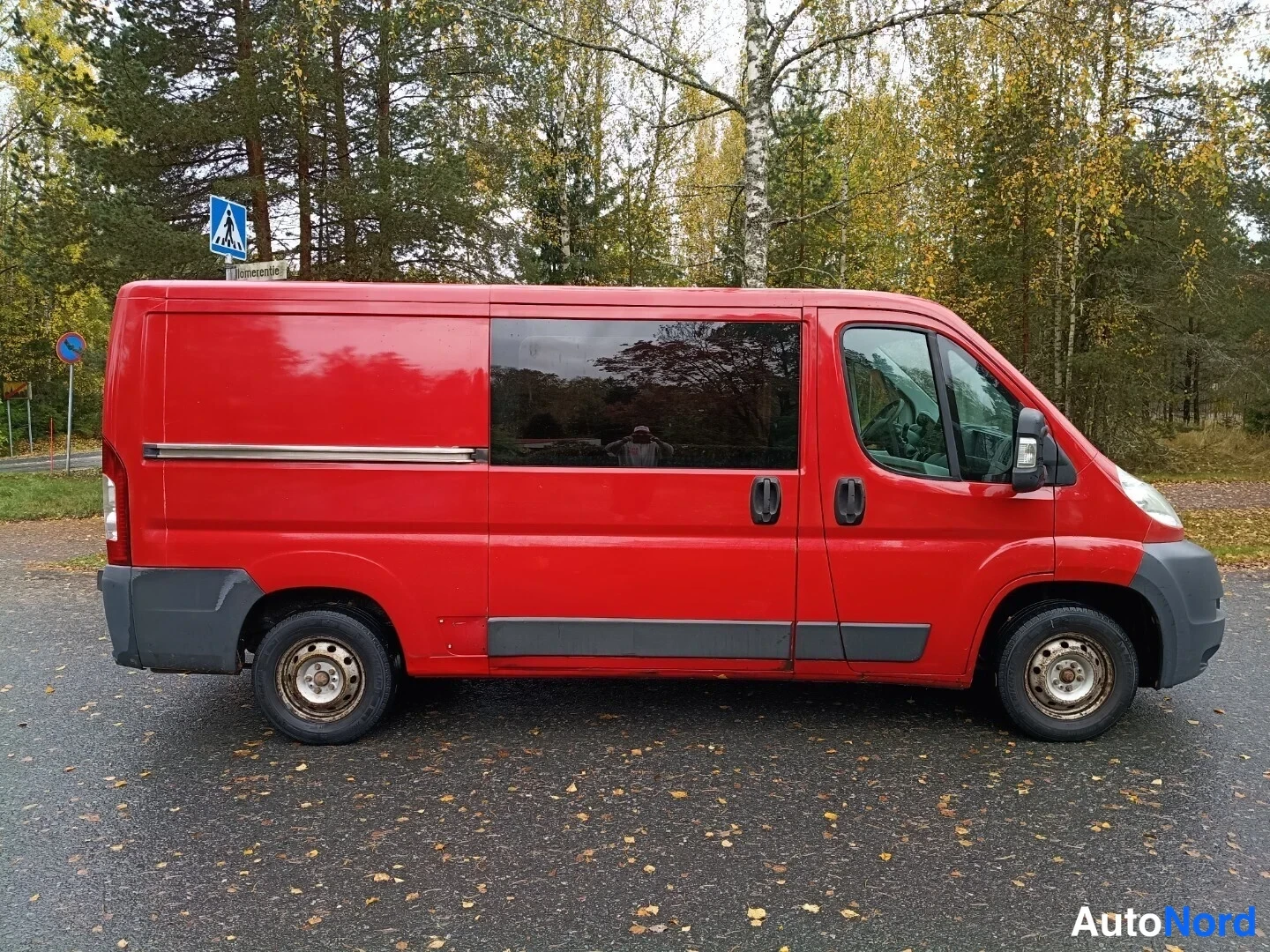Sivulta: Punaisen pakettiauton sivuprofiili vasemmalta sivulta, auton keula osoittaa oikealle.
