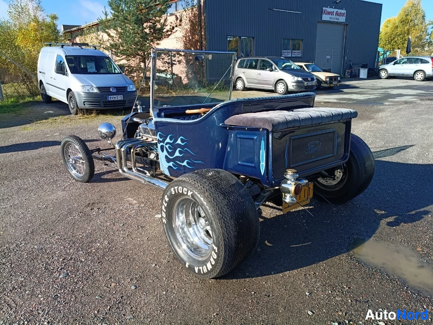 Takaviisto: Ford T-bucket takaa ja vasemmalta sivulta nähtynä, takakori ja verstasrakennus taustalla.