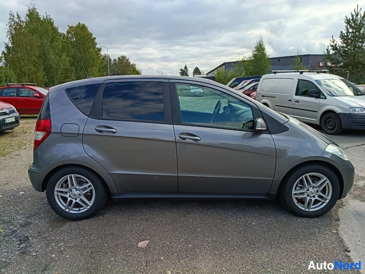 Sivulta: Harmaa Mercedes-Benz A -henkilöauto sivulta kuvattuna pysäköintialueella, hopeavanteet.