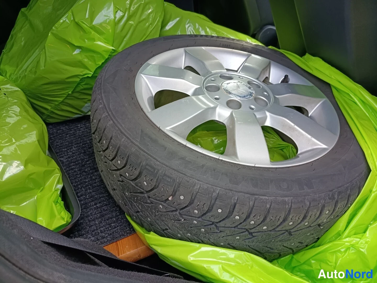 Muu: Talvirenkaita ja Mercedes-merkitty alumiinivanne autoon tavaratilassa vihreiden muovipussien päällä.