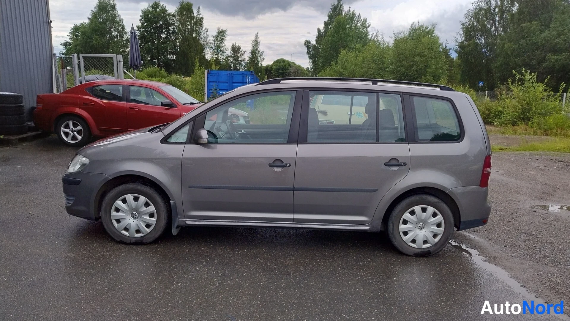 Etuviisto, nokka vasemmalle: Volkswagen Touran sivulta vasemmalta katsottuna; kattokaiteet, ovet ja kolmen renkaan vanteet näkyvät.