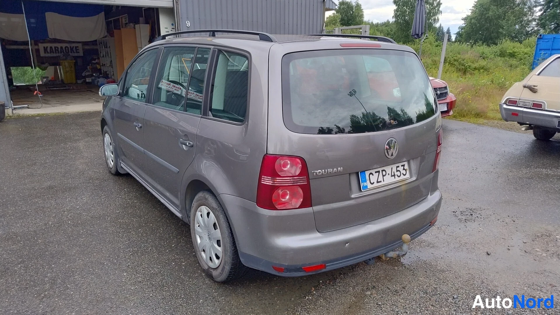 Takaviisto: Volkswagen Touran takaa vinosti; TOURAN-merkintä, rekisterikilpi, takavetoaisa ja kattokaiteet näkyvät.