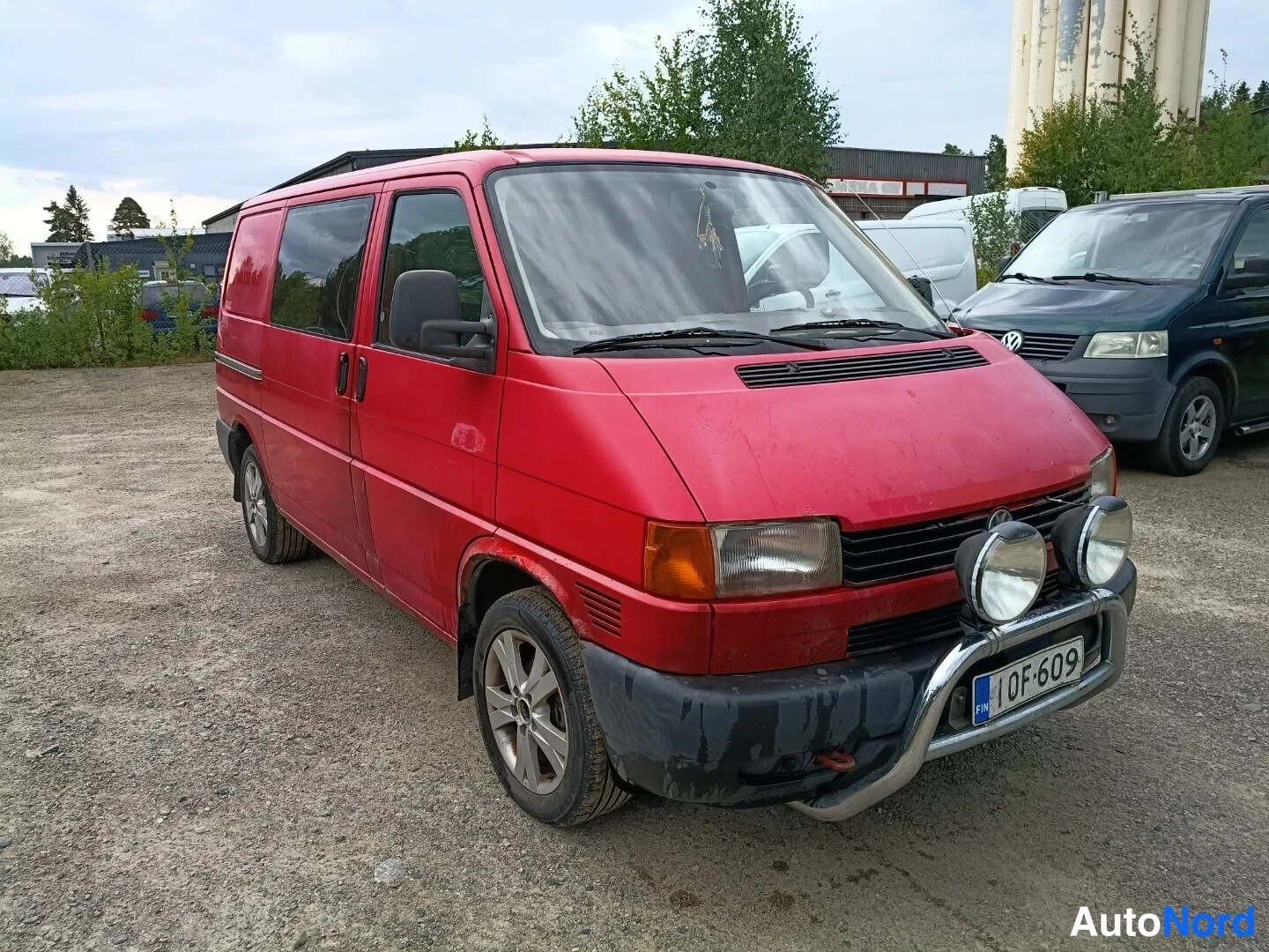 Etuviisto, nokka oikealle: Punainen Volkswagen Transporter etukulmasta oikealta, keulakaari ja lisävalot, rekisteritunnus 1OF-609.