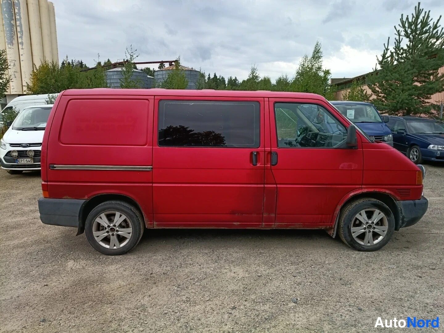 Sivulta: Punainen Volkswagen Transporter -pakettiauto sivulta kuvattuna, koko ajoneuvo näkyvissä.