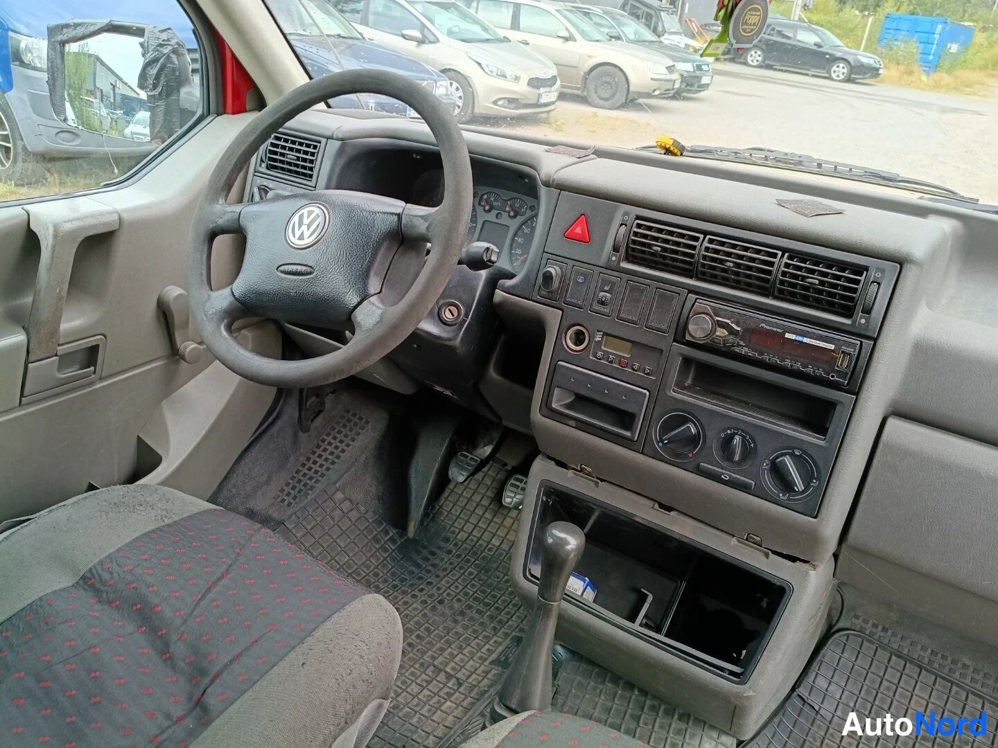 Muu: Volkswagen Transporterin ohjaamo sisältä: Volkswagen-ohjauspyörä, kojelauta, manuaali vaihteenvalitsin ja radiopaneeli näkyvät.