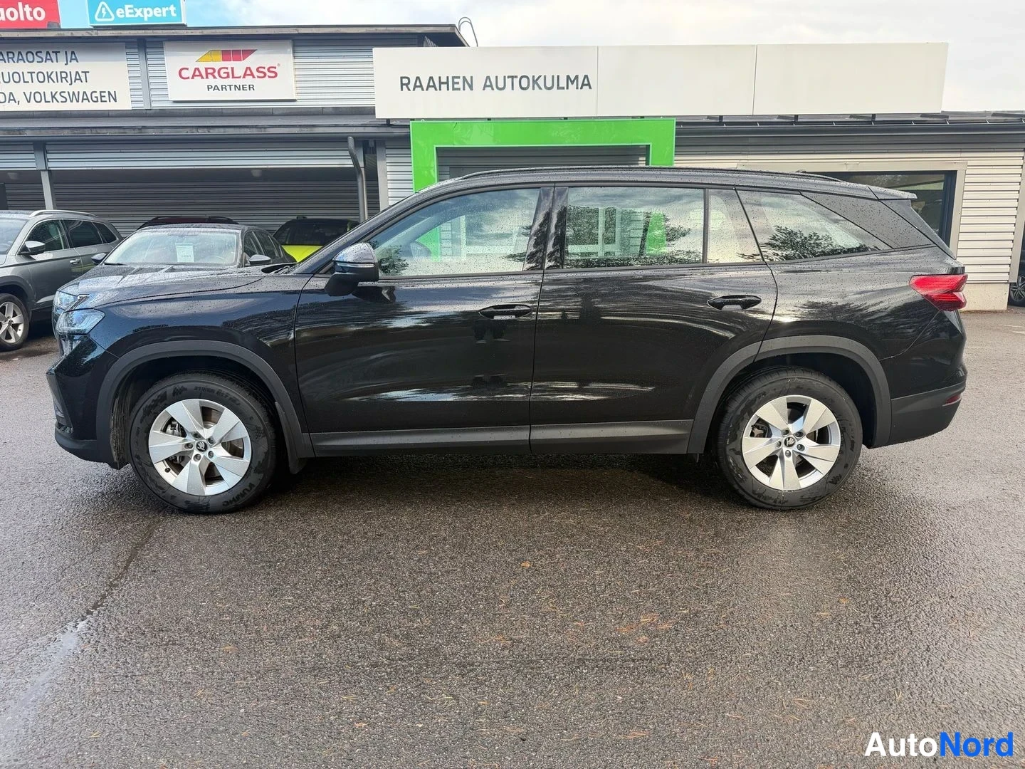 Sivulta: Mustan Skoda Kodiaq -maasturin sivuprofiili vasemmalta sivulta, autopaikalla autoliikkeen edessä.