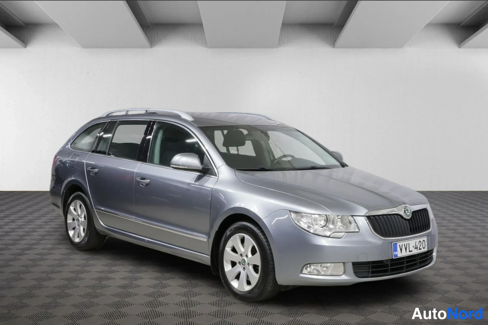 Etuviisto, nokka oikealle: Skoda Superb -farmariauto edestä sivusta, keulakoriste ja rekisteri näkyvissä.