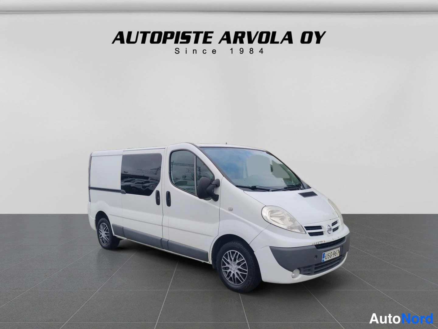 Etuviisto, nokka oikealle: Valkoinen Nissan Primastar -pakettiauto etukulmasta oikealta, studiovalkoinen tausta.