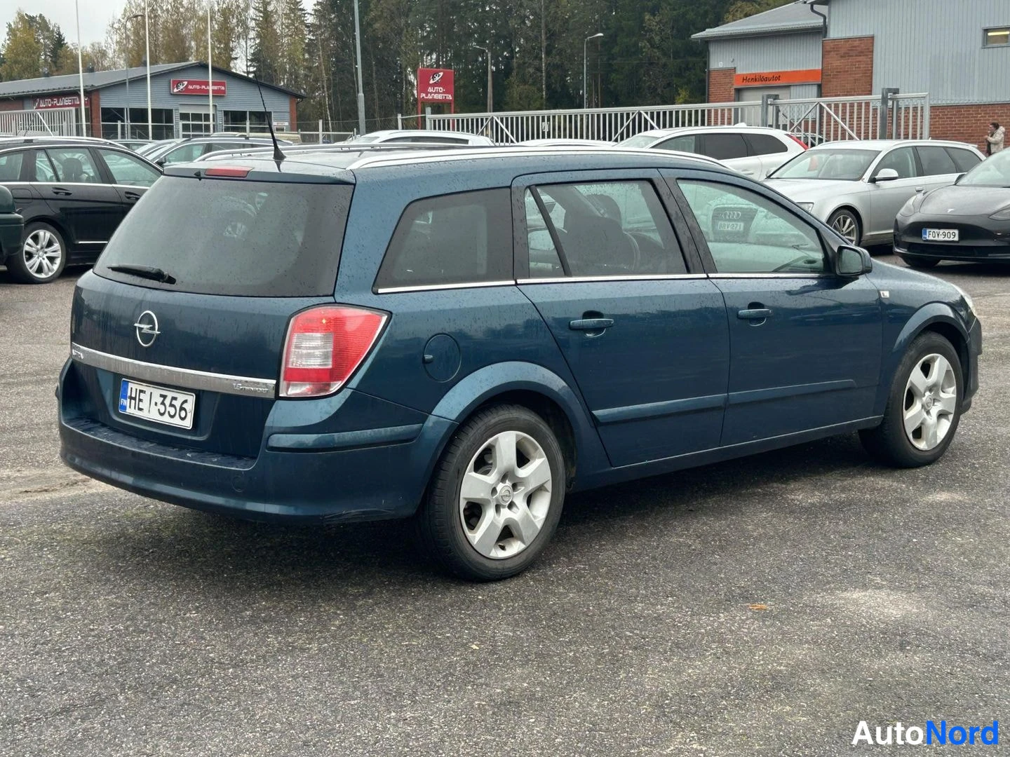 Takaviisto: Takaapikulmassa kuvattu tummansininen farmariauto parkkipaikalla, rekisterikilpi.