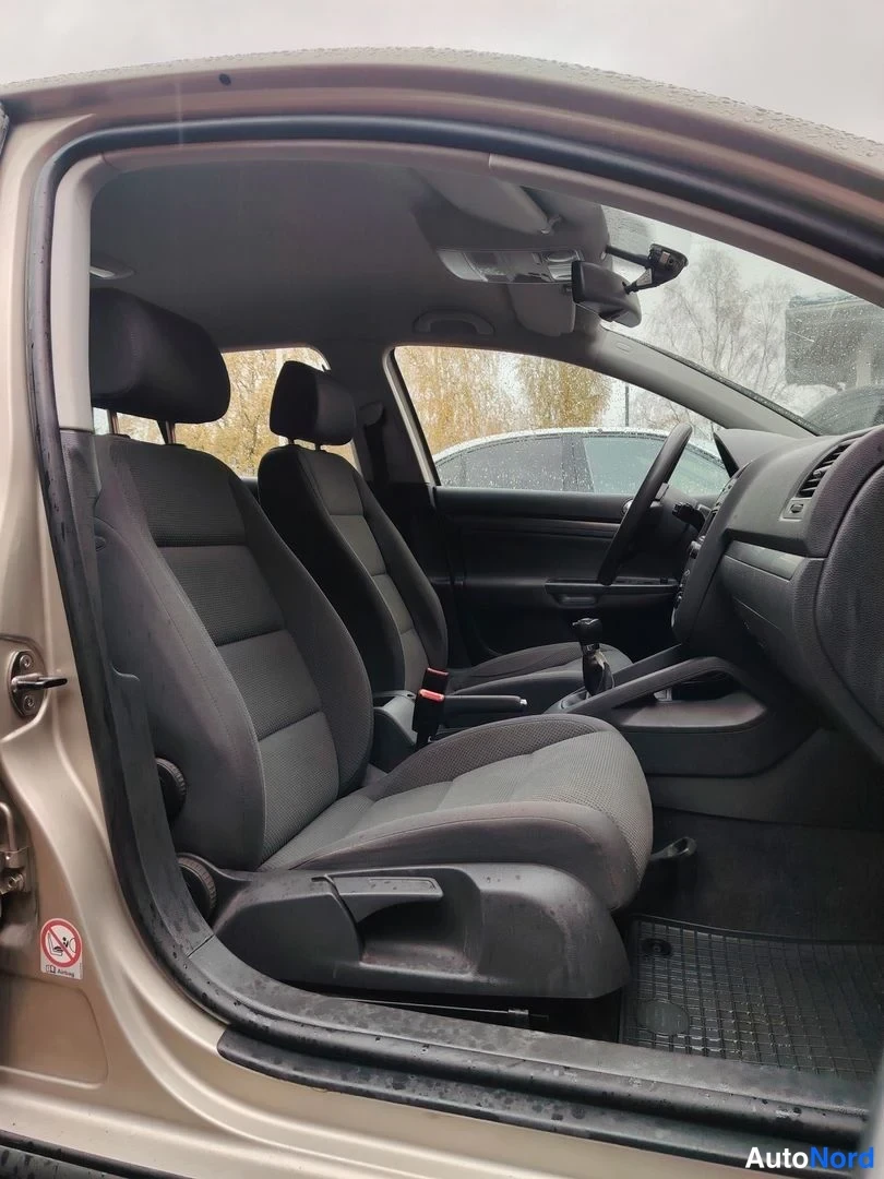 Etuviisto, nokka oikealle: Näkymä Volkswagen Golfin sisätiloihin etumatkalta taakse: harmaat etuistuimet, käsijarru ja vaihteenvalitsin, kuljettajan ovi auki.