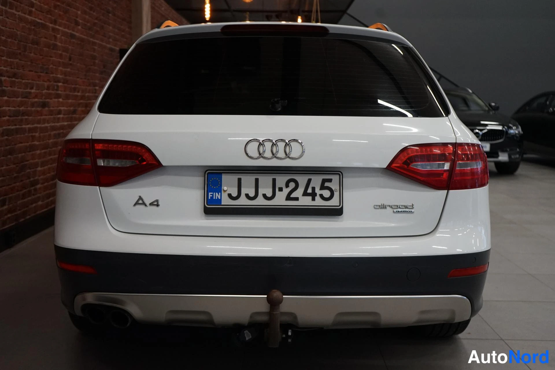 Takaa: Auton takanäkymä: valkoinen Audi A4 allroad, Audi-renkaat, rekisterikilpi ja vetokoukku.