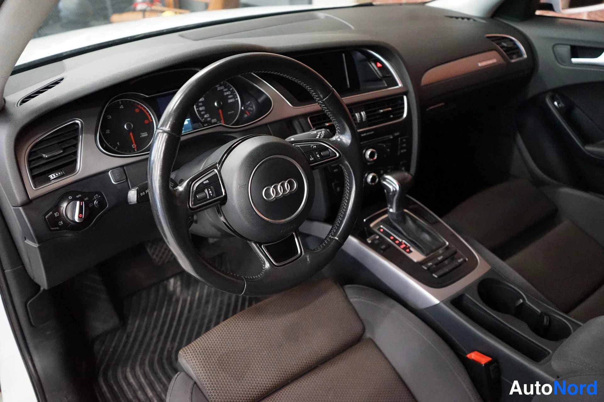 Edestä: Matkustamon näkymä: Audi-ohjauspyörä, mittaristo ja automaattivaihteen vipu.