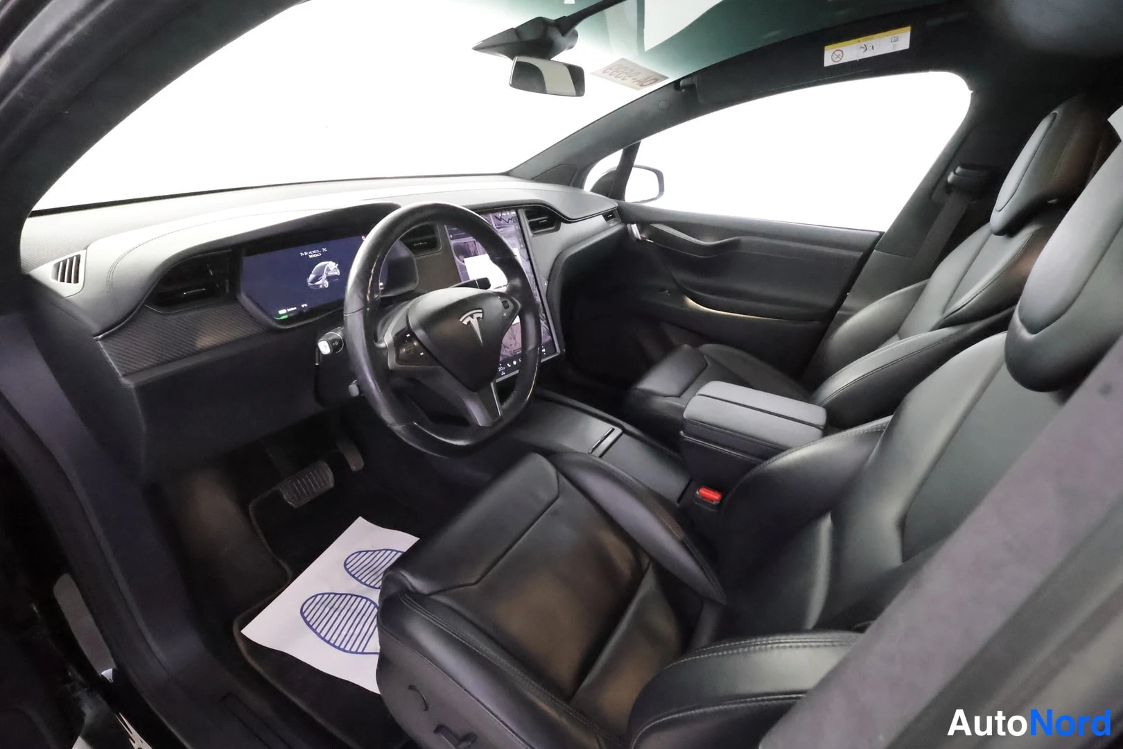 Edestä: Mustan Tesla Model X:n matkustamoon näkyy ohjauspyörä, keskinäytön infotainmentjärjestelmä ja nahkaiset istuimet.