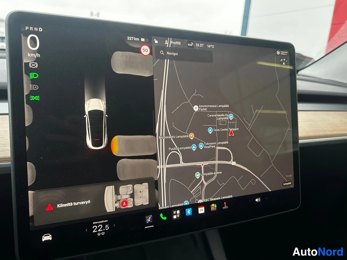 Yksityiskohta: Tesla Model Y:n keskinäyttö pysäköidyssä autossa: vasemmalla P-vaihde, nopeus 0 km/h, huomio 'Kiinnitä turvavyö' ja 227 km:n toimintasäde, oikealla kartta Lempä