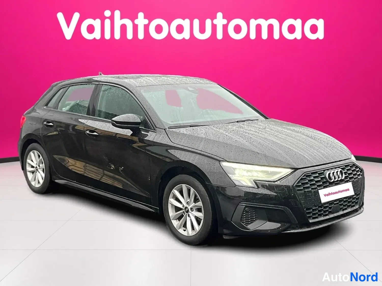 Etuviisto, nokka oikealle: Musta Audi A3 Sportback -viististä etualaa vasemmalta kuvattuna sadevesipisaroin peittyneenä.