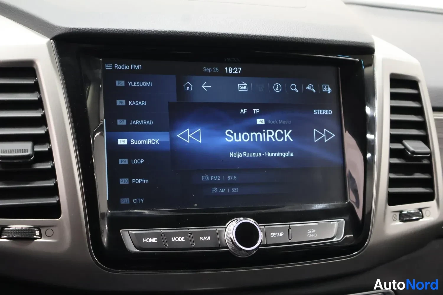 Muu: Keskikonsolin infotainment-näyttö radionäkymässä (Radio FM1, kanava SuomiRCK 87.5, kello 18:27), alapuolella HOME-, MODE-, NAVI-, SETUP- ja CARD-painikkeet.