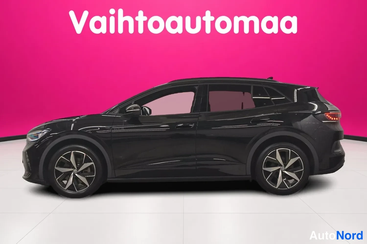 Sivulta: Mustan Volkswagen ID.4:n sivukuva vasemmalta, kokonainen kylki ja pyörät näkyvissä katetussa autosalissa.